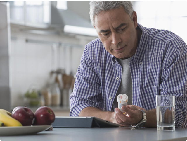 Man looking away from his tablet to read a prescription bottle label