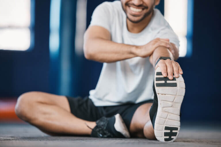 Foot, exercise and stretching with a sports man in the gym getting ready for a cardio training routine. Fitness, health and warm up with a male athlete in preparation of a workout for wellness.