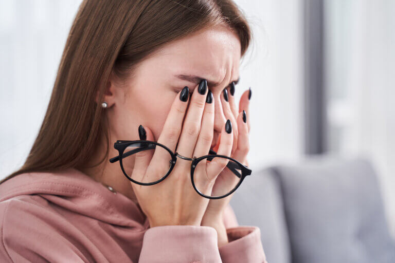 Portrait view of tired young woman feeling pain eyestrain and rubbing dry irritated eyes while sitting at the sofa after hardworking with her laptop.