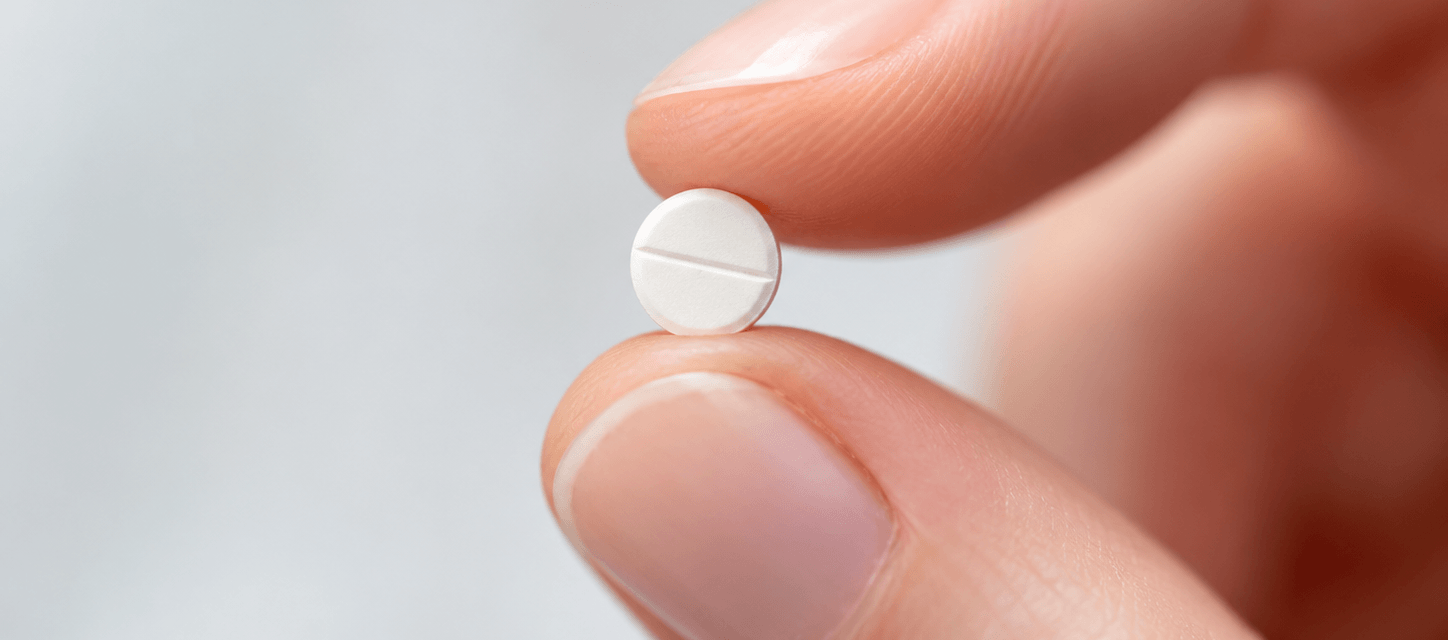 Small, white, scored tablet held between two fingertips, highlighting its compact size.